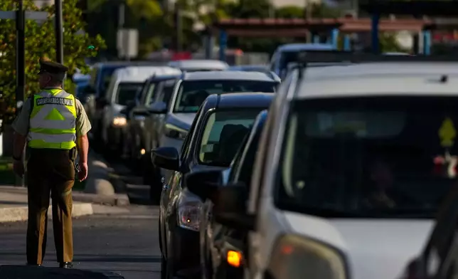 A police officer directs drivers lining up to fill their tanks with fuel in Santiago, Chile, Tuesday, March 24, 2026. (AP Photo/Esteban Felix)