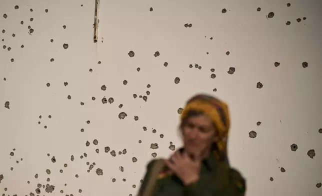 A member of the armed wing of the Kurdish-Iranian opposition group Organization of Iranian Kurdistan Struggle, known as Khabat, stands in front of a shrapnel pockmarked wall that allegedly was damaged in strike by Iranian-backed militias in Iraq last week at a military base on the outskirts of Irbil, Iraq, Monday, March 16, 2026. (AP Photo/Leo Correa)