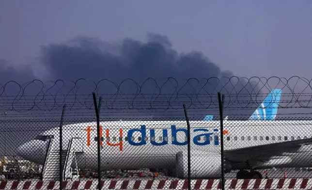 A FlyDubai plane is parked at Dubai International Airport as smoke rises in the background after a drone struck a fuel tank early morning, forcing the temporary suspension of flights, in Dubai, United Arab Emirates, Monday, March 16, 2026. (AP Photo)