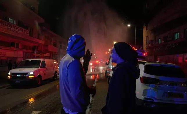 Residents look on as first responders work at the site of a missile strike in Tel Aviv, Israel, early Saturday, March 28, 2026. (AP Photo/Maya Levin)