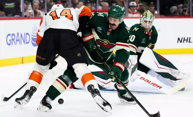 Minnesota Wild defenseman Jake Middleton (5) knocks the puck away from Philadelphia Flyers center Sean Couturier (14) during the second period of an NHL hockey game Thursday, March 12, 2026, in St. Paul, Minn. (AP Photo/Ellen Schmidt)