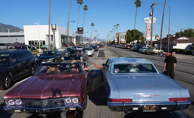 Sandy Avila, left, driving a 1966 Chevy Impala SS, high-fives a fellow lowrider at the 6th Annual Lady Lowrider Cruise Night in celebration of International Women's Day in Pasadena, Calif., on Sunday, March 8, 2026. (AP Photo/Damian Dovarganes)