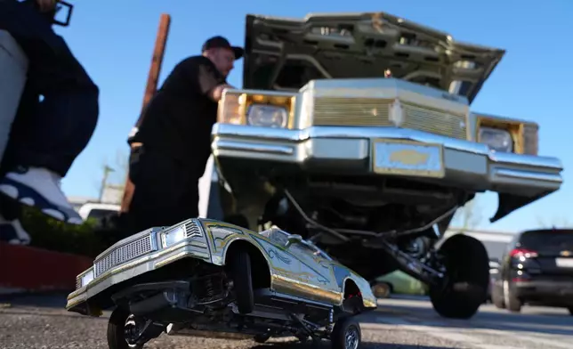A toy lowrider is placed under a real one at the 6th Annual Lady Lowrider Cruise Night in celebration of International Women's Day in Pasadena, Calif., on Sunday, March 8, 2026. (AP Photo/Damian Dovarganes)