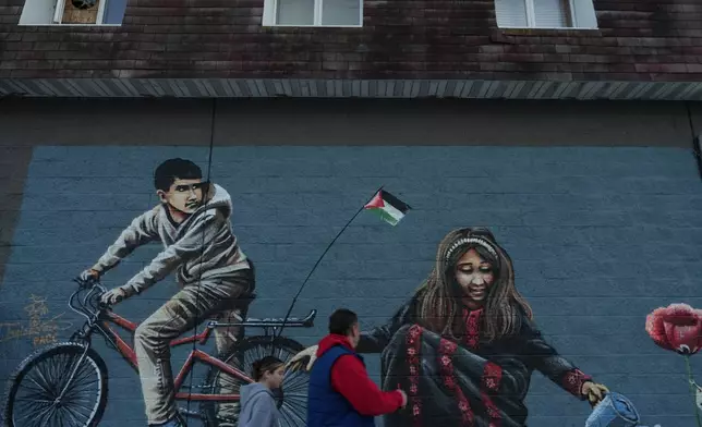 Passersby walk in front of a mural in "Palestine Way," a section of Main Street in the South Paterson neighborhood of Paterson, N.J. during Ramadan on Friday, Feb. 27, 2026. (AP Photo/Luis Andres Henao)