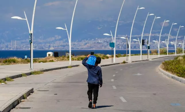 FILE - A young street vendor carries a pack of water bottles as he looking for customers during a sweltering day on the Mediterranean Sea corniche in Beirut, Lebanon, July 20, 2023. (AP Photo/Hassan Ammar, File)