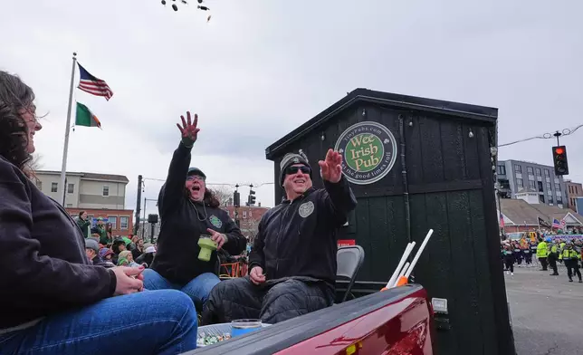 Dena Taylor and Tony DiDonato, right, toss candy to spectators while riding in a truck hauling the "Wee Irish Pub", a fully functioning mobile Irish pub built by two Massachusetts' brothers, during the annual St. Patrick's Day parade through the South Boston neighborhood, Sunday, March 15, 2026. (AP Photo/Charles Krupa)