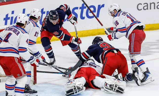 New York Rangers goaltender Igor Shesterkin (31) saves the shot from Winnipeg Jets' Mark Scheifele (55) as he gets knocked over by Jets' Cole Perfetti (91) during the first period of an NHL game in Winnipeg, Thursday, March 12, 2026. (John Woods/The Canadian Press via AP)