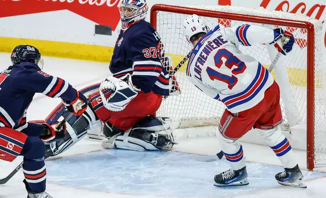 New York Rangers' Alexis Lafreniere's (13) shot just goes over the net behind Winnipeg Jets goaltender Connor Hellebuyck's (37) as Dylan Samberg (54) defends during the first period of an NHL game in Winnipeg, Thursday, March 12, 2026. (John Woods/The Canadian Press via AP)