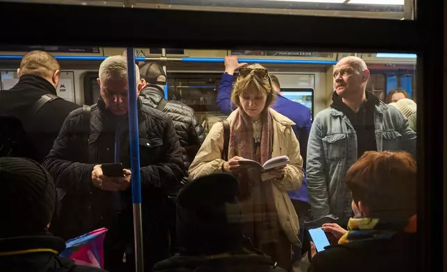 A man looks at his smartphone as a woman reads a book while on the subway in Moscow Thursday, March 12, 2026. (AP Photo/Alexander Zemlianichenko)