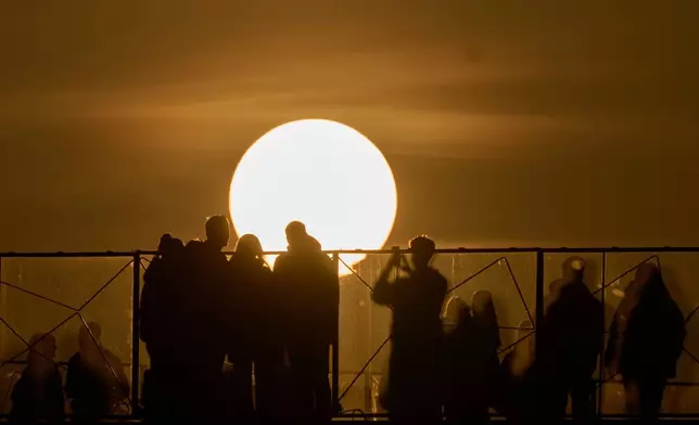 People watch and take photos during sunset in Moscow, Thursday, March 12, 2026. (AP Photo/Alexander Zemlianichenko)