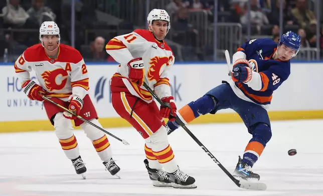 New York Islanders defenseman Matthew Schaefer (48) passes the puck around Calgary Flames center Mikael Backlund (11) during the second period of an NHL hockey game, Saturday, March 14, 2026, in Elmont, N.Y. (AP Photo/Heather Khalifa)