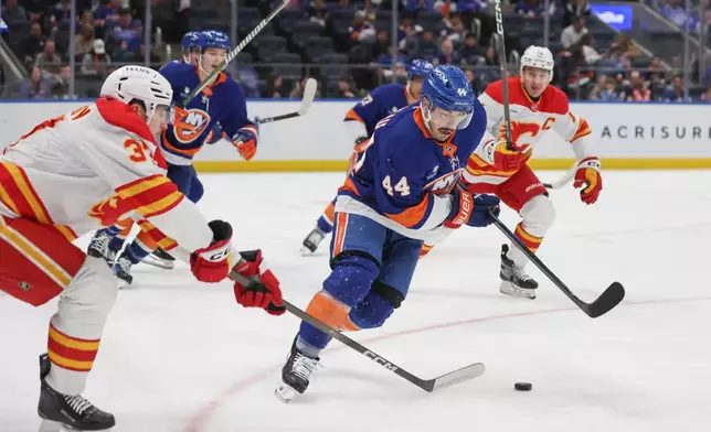 New York Islanders center Jean-Gabriel Pageau (44) takes the puck from Calgary Flames defenseman Yan Kuznetsov, left, during the first period of an NHL hockey game, Saturday, March 14, 2026, in Elmont, N.Y. (AP Photo/Heather Khalifa)