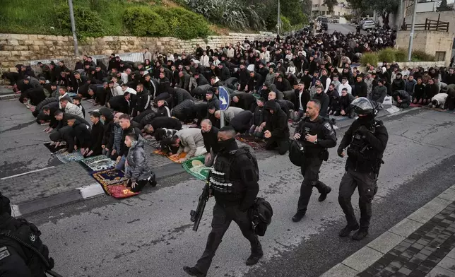 Israeli police officers pass by Palestinian Muslims as they offer Eid al-Fitr prayers in Jerusalem while the Old City remains closed to visitors under nationwide Home Front Command restrictions banning large gatherings amid the war with Iran, Friday, March 20, 2026. (AP Photo/Mahmoud Illean)