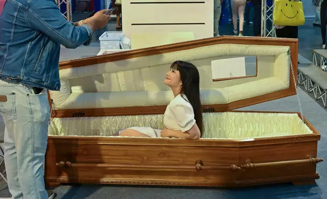 A visitor poses for a photo sitting in a coffin at Death Fest in Nonthaburi, Thailand, Friday, March 13, 2026. (AP Photo/Kittinun Rodsupan)