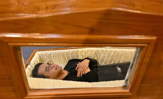 A visitor tries out a coffin at Death Fest in Nonthaburi, Thailand, Friday, March 13, 2026. (AP Photo/Kittinun Rodsupan)