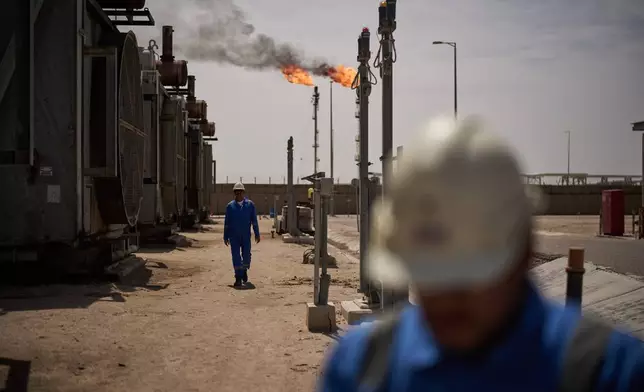 Workers walk in an area at a degassing station in Zubair oil field, whose operations have being reduced due to the Mideast war triggered by the U.S. and Israeli attacks on Iran, near Basra, Iraq, Saturday, March 28, 2026. (AP Photo/Leo Correa)
