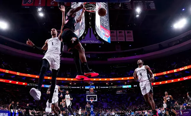 Philadelphia 76ers' VJ Edgecombe, center, dunks the ball as San Antonio Spurs' Victor Wembanyama, left, comes over to defend during the first half of an NBA basketball game, Tuesday, March 3, 2026, in Philadelphia. (AP Photo/Chris Szagola)