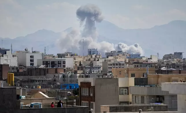 People watch from a rooftop as a plume of smoke rises after a strike in Tehran, Iran, Sunday, March 1, 2026. (AP Photo/Vahid Salemi)