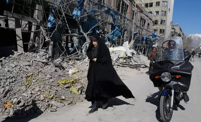 A woman walks past a building which was damaged after a strike on a police station amid the U.S.–Israeli military campaign in Tehran, Iran, Tuesday, March 3, 2026. (AP Photo/Vahid Salemi)