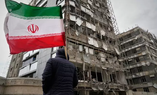A man holds an Iranian flag as he looks at the damaged façade of Gandhi Hospital, which was hit Sunday when a strike also struck a state TV communications tower and nearby buildings across the street during the ongoing joint U.S.–Israeli military campaign in Tehran, Iran, Monday, March 2, 2026. (AP Photo/Vahid Salemi)