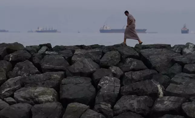 A man walks along the shore as oil tankers and cargo ships line up in the Strait of Hormuz, as seen from Khor Fakkan, United Arab Emirates, Wednesday, March 11, 2026. (AP Photo/Altaf Qadri)