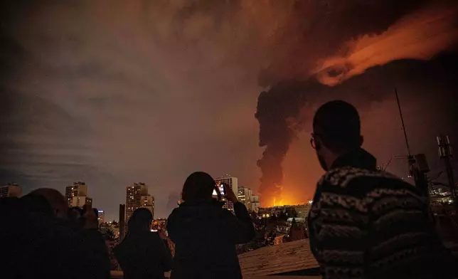 Residents look on and take pictures as flames and smoke rise from an oil storage facility struck as attacks hit the city during the U.S.–Israeli military campaign in Tehran, Iran, Saturday, March 7, 2026. (Alireza Sotakbar/ISNA via AP)