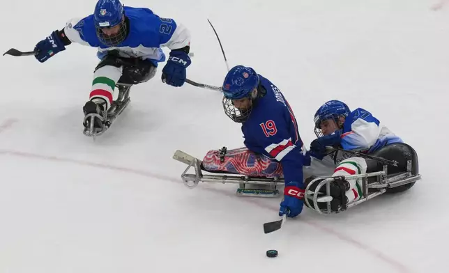 United States' Malik Jones, centre, challenges for the puck with Italy's Eusebiu Antochi, left, and Italy's Alessandro Andreoli during the Group A hockey match between United States and Italy at the 2026 Winter Paralympics, in Milan, Italy, Saturday, March 7, 2026. (AP Photo/Antonio Calanni)