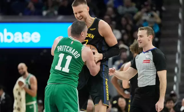 Golden State Warriors center Kristaps Porziņģis, top, smiles while wrestling for the ball with Boston Celtics guard Payton Pritchard (11) as referee Brandon Schwab watches during the second half of an NBA basketball game in San Francisco, Thursday, Feb. 19, 2026. (AP Photo/Jeff Chiu)