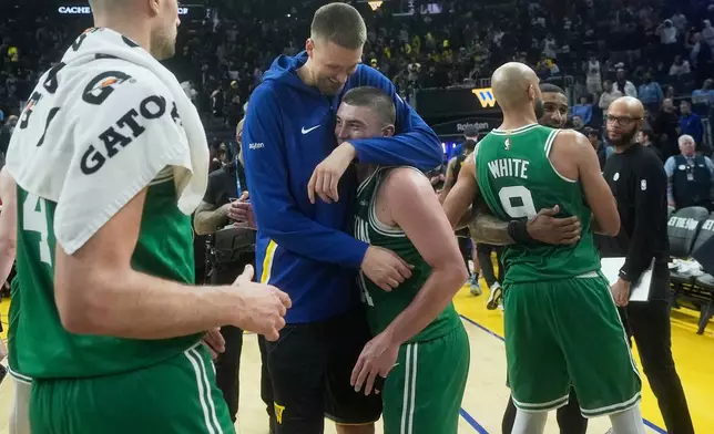 Golden State Warriors center Kristaps Porziņģis, top middle, hugs Boston Celtics guard Payton Pritchard as Celtics guard Derrick White (9) hugs Warriors guard Gary Payton II after an NBA basketball game in San Francisco, Thursday, Feb. 19, 2026. (AP Photo/Jeff Chiu)