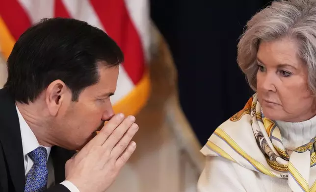 Secretary of State Marco Rubio, left, whispers to White House chief of staff Susie Wiles during a roundtable discussion on college sports in the East Room of the White House, Friday, March 6, 2026, in Washington. (AP Photo/Julia Demaree Nikhinson)