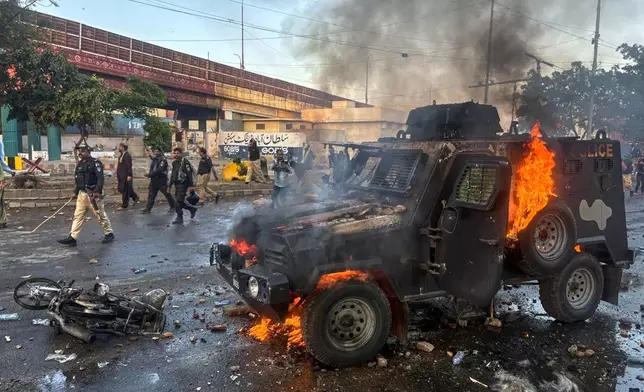 Paramilitary soldiers and police officers walk past a burning police's armoured vehicle, which was set on fire by Shiite Muslims during a protest over the killing of Iranian Supreme Leader Ayatollah Ali Khamenei, in Karachi, Pakistan, Sunday, March 1, 2026. (AP Photo/Muhammad Farooq)