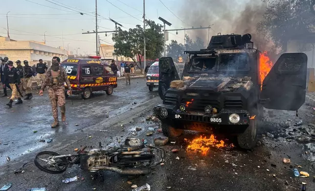 Paramilitary soldiers and police officers walk past a burning police's armoured vehicle, which was set on fire by Shiite Muslims during a protest over the killing of Iranian Supreme Leader Ayatollah Ali Khamenei, in Karachi, Pakistan, Sunday, March 1, 2026. (AP Photo/Muhammad Farooq)