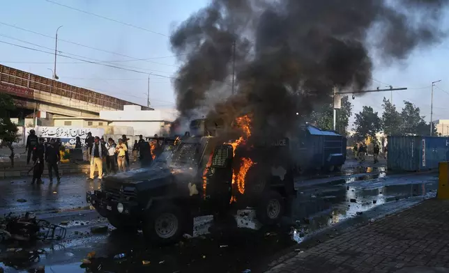 Police officers walk past a burning police's armoured vehicle, which was set on fire by Shiite Muslims during a protest to condemn the killing of Iranian Supreme Leader Ayatollah Ali Khamenei, in Karachi, Pakistan, Sunday, March 1, 2026. (AP Photo/Ali Raza)