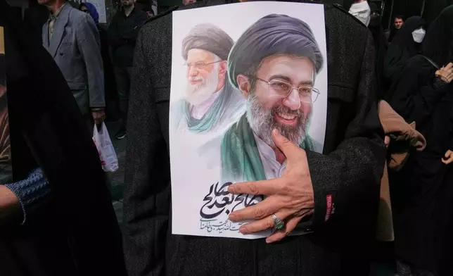 A mourner holds a poster depicting Ayatollah Mojtaba Khamenei, right, the successor to his late father Ayatollah Ali Khamenei, left, as supreme leader, during the funeral procession for senior Iranian military officials and civilians killed during the U.S.-Israel campaign in Tehran, Iran, Wednesday, March 11, 2026. (AP Photo/Vahid Salemi)