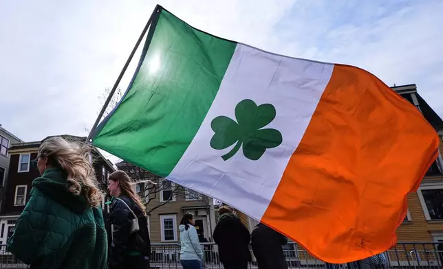 A spectator walks with an Irish shamrock flag during the annual St. Patrick's Day parade through the South Boston neighborhood, Sunday, March 15, 2026, in Boston. (AP Photo/Charles Krupa)