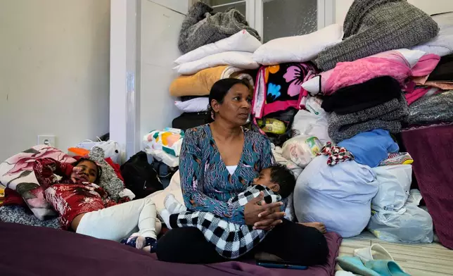 A displaced migrant woman, who among many others who fled Israeli strikes in southern and eastern Lebanon and Beirut's southern suburbs, sits with her children on mattresses at Saint Joseph Church, which has been turned into a shelter for displaced migrants, mostly from African nations, in Beirut, Wednesday, March 11, 2026. (AP Photo/Hussein Malla)
