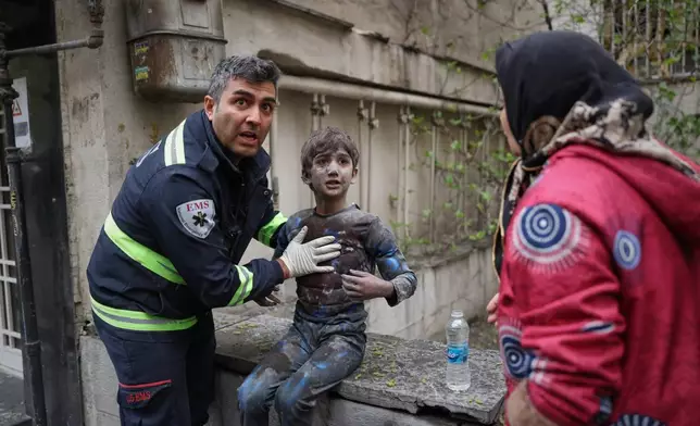 A first responder assists an injured boy following a strike that hit a residential building amid the U.S.-Israeli military campaign in Tehran, Iran, Saturday, March 28, 2026. (AP Photo/Sajad Safari)