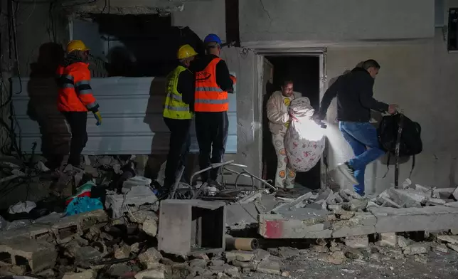 Residents carry personal belongings as they leave a building damaged in a missile strike in Tel Aviv, Israel, early Saturday, March 28, 2026. (AP Photo/Maya Levin)