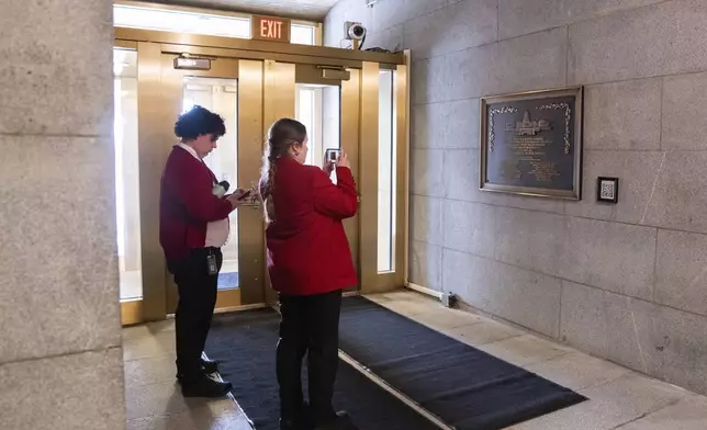 Capitol tour guides take photos of a plaque honoring police service on Jan. 6, 2021 at the Capitol, Saturday, March 7, 2026, in Washington. (AP Photo/Allison Robbert)