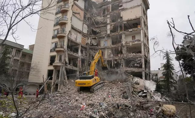 Iranian firefighters use an excavator to clear rubble from a residential building that was hit in an earlier U.S.-Israeli strike in Tehran, Iran, Monday, March 23, 2026. (AP Photo/Vahid Salemi)