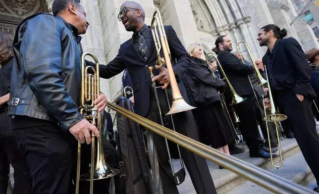A group of musicians, primarily trombonists, socialize and warm-up pose before playing at a funeral for Willie Colon at St. Patrick's Cathedral in New York, Monday, March 9, 2026. (AP Photo/Seth Wenig)