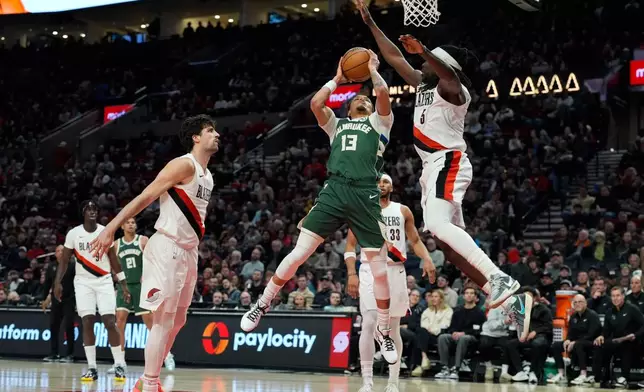 Milwaukee Bucks guard Ryan Rollins (13) goes to the basket past Portland Trail Blazers guard Jrue Holiday (5) during the first half of an NBA basketball game Wednesday, March 25, 2026, in Portland, Ore. (AP Photo/Jenny Kane)