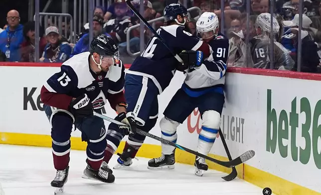 Colorado Avalanche right wing Valeri Nichushkin, left, collects the puck as defenseman Brent Burns, back left, checks Winnipeg Jets center Cole Perfetti (91) in the second period of an NHL hockey game Saturday, March 28, 2026, in Denver. (AP Photo/David Zalubowski)
