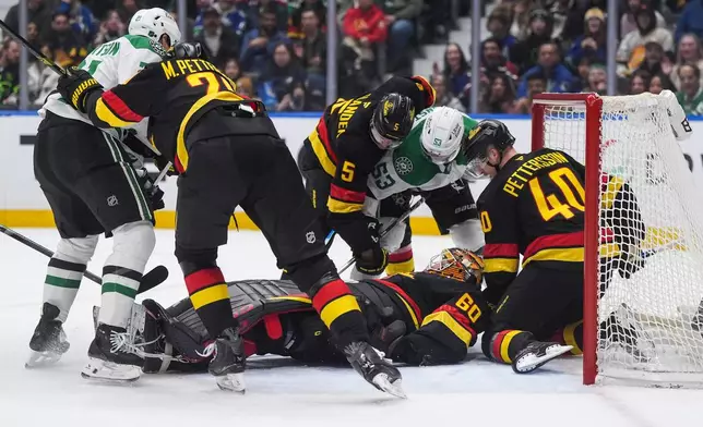 Vancouver Canucks goalie Nikita Tolopilo (60) lies on the puck as teammates Elias Pettersson (40), Tom Willander (5) and Marcus Pettersson (29) defend against Dallas Stars' Wyatt Johnston (53) and Jason Robertson (21), left, during the first period of an NHL hockey game in Vancouver, British Columbia, Monday, March 2, 2026. (Darryl Dyck/The Canadian Press via AP)