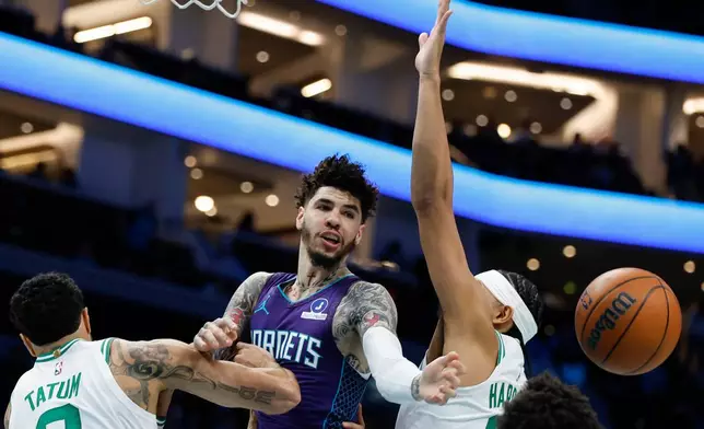Charlotte Hornets guard LaMelo Ball, center, passes between Boston Celtics forward Jayson Tatum (0) and guard Ron Harper Jr. during the first half of an NBA basketball game in Charlotte, N.C., Sunday, March 29, 2026. (AP Photo/Nell Redmond)