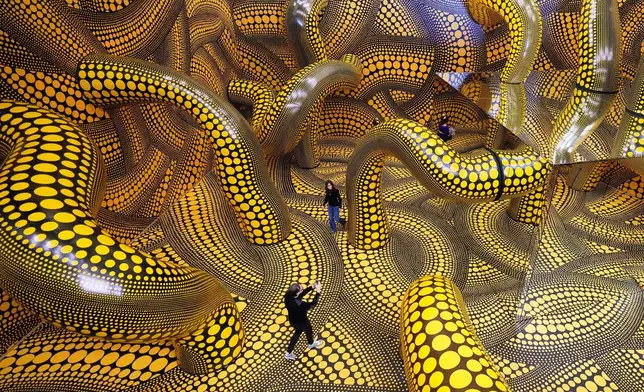 People walk through the artwork 'Infinity Mirrored Room' during a preview of the new major exhibition of legendary Japanese artist Yayoi Kusama at the Museum Ludwig in Cologne, Thursday, March 12, 2026. (AP Photo/Martin Meissner)