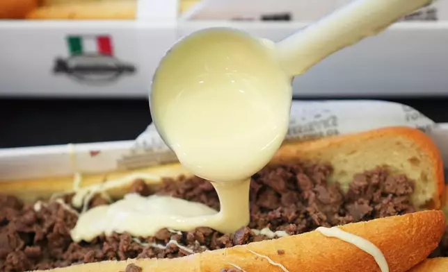 A volunteer ladles out cheese onto one of many cheesesteaks as part of a Guinness World Record attempt on National Cheesesteak Day at Philadelphia International Airport, in Philadelphia, Tuesday, March 24, 2026, in Philadelphia. (AP Photo/Matt Rourke)