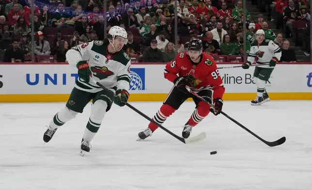 Minnesota Wild defenseman Quinn Hughes, left, and Chicago Blackhawks wing Ilya Mikheyev (95) go for the puck during the first period of an NHL hockey game, Tuesday, March, 17, 2026, in Chicago. (AP Photo/David Banks)