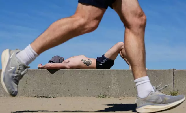 A jogger runs past as a man sunbathes at Crissy Field in San Francisco, Tuesday, March 17, 2026. (AP Photo/Godofredo A. Vásquez)