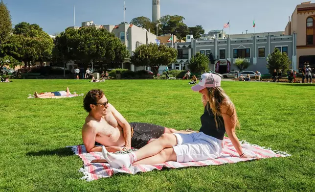 Nick Gardetto, left, and Madi Hirsch lounge in the sun at Washington Square during a heat wave in San Francisco, Sunday, March 15, 2026. (Brontë Wittpenn/San Francisco Chronicle via AP)
